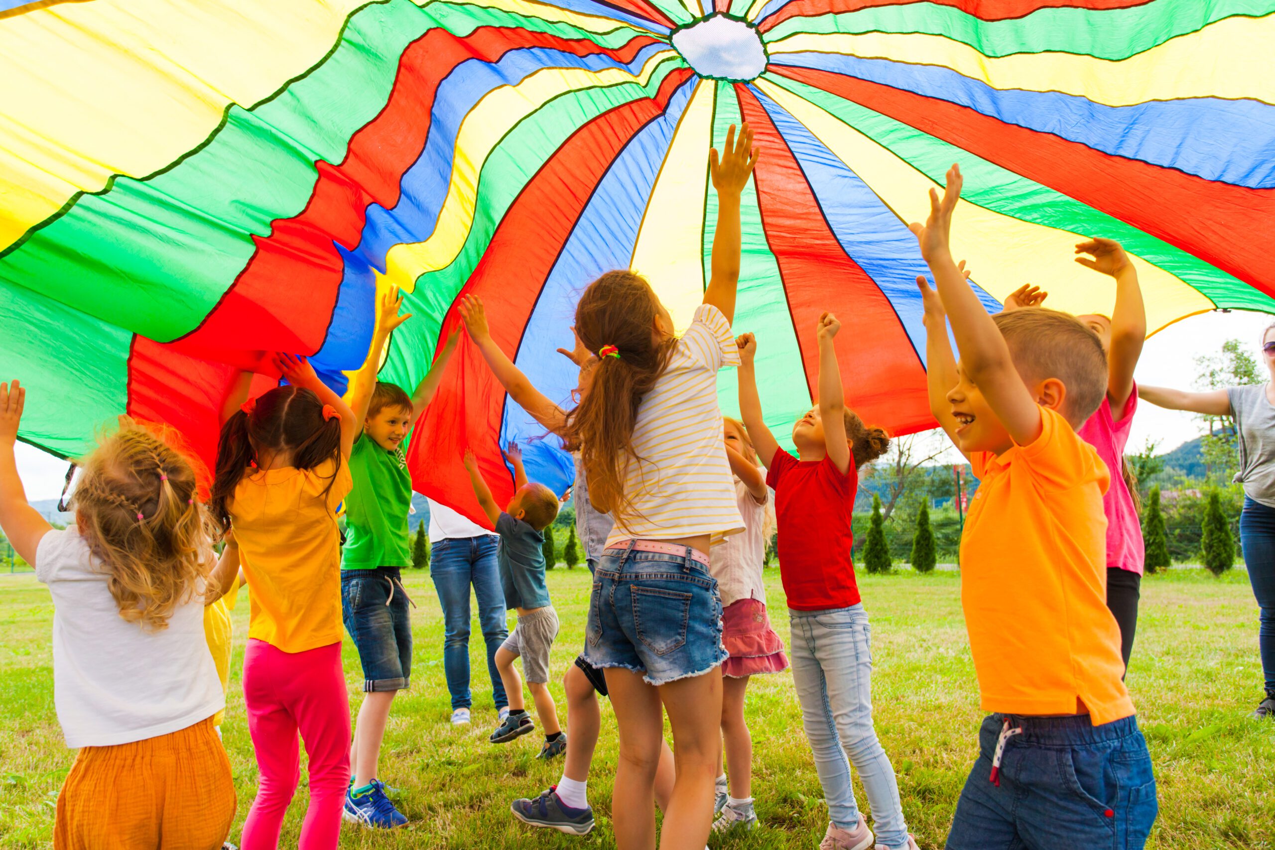 kids at summer camp play under colorful parachute